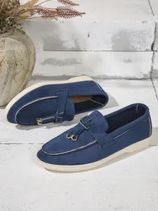 Close-up of blue suede flat loafers with gold metal buckle on textured background