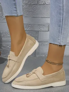 Close-up detail of beige suede flat loafers with metal ring accent and slip-on design