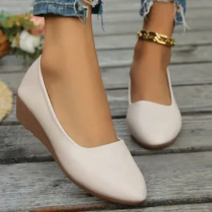 Primer plano de elegantes zapatos de cuña beige con punta fina para mujer sobre madera rústica.
