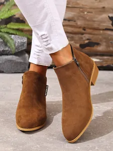 Detailopname van bruine suède Chelsea boots met puntige neus, zijrits en een stevige blokhak.
