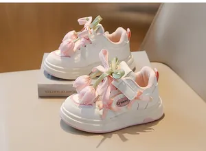Gros plan de baskets blanches pour enfants avec tulipes en tissu rose et rubans.