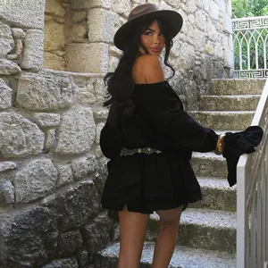 Close-up view of a model wearing a black off-the-shoulder dress on stone stairs outdoors