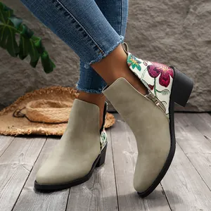 Botines con bordados florales y tacón grueso sobre un suelo de madera de estilo rústico.