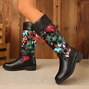 Close-up of black women's knight boots featuring vibrant floral embroidery and metal buckle.