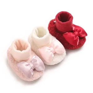 Soft plush baby girl booties with large satin bows in pink, cream, and red colors.