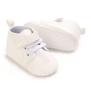 Close-up detail of white infant baptism shoes featuring elegant embroidered cross design.