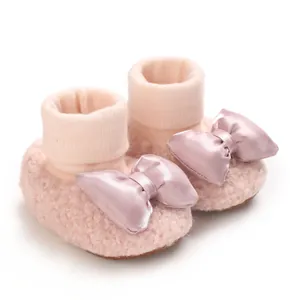 Close-up detail of soft pink fleece-lined baby booties with a decorative satin bow accent.