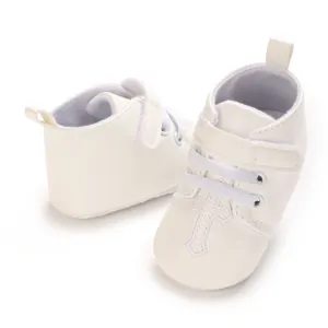 Detail of white baptism baby shoes with cross embroidery and velcro strap.