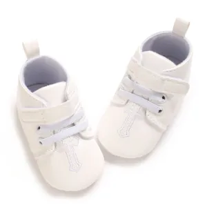 Detailed view of white leather baby christening shoes with embroidered cross and Velcro strap