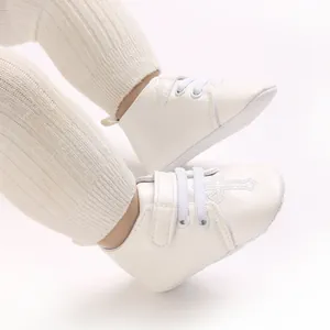 Close-up of white infant christening shoes featuring elegant cross embroidery detail