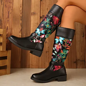 Detail of black leather riding boots with colorful floral embroidery and buckle strap