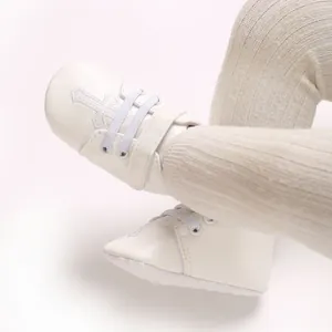 Close-up of white baby baptism shoes with cross embroidery and knitted leggings