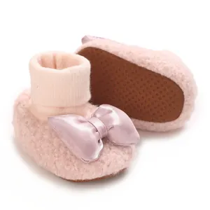 Close-up of pink plush baby booties featuring a large satin bow and non-slip sole detail