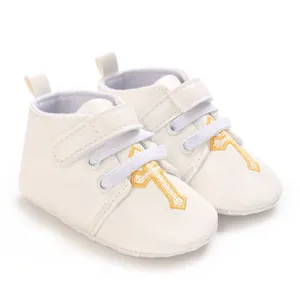 Detailed view of white faux leather baby christening shoes with golden cross embroidery