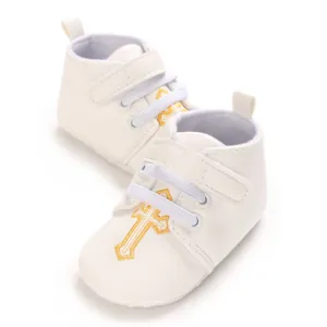 Close-up detail of white infant baptism shoes with elegant gold cross embroidery design