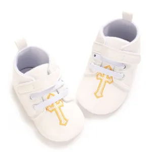 Close-up of white baptism baby shoes with golden embroidered cross detail and velcro strap.
