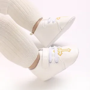 Close-up of white soft-soled baptism baby shoes featuring golden cross embroidery