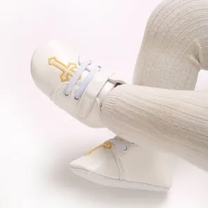 Detail view of white infant baptism shoes with embroidered yellow cross pattern.