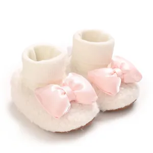Close-up of white fleece baby shoes featuring a decorative pink satin bow