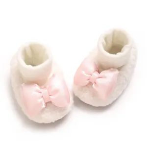 Close-up of white plush baby booties featuring a delicate pink satin bow design