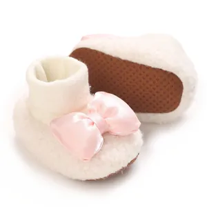 Close-up of white fluffy baby booties with a pink satin bow and non-slip soles