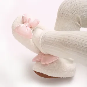 Detailed view of cozy white fleece baby walking shoes with pink satin bow decoration