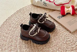 Detailansicht brauner Mädchen-Lederschuhe mit Spitzenbesatz und Schleife auf Teppich.