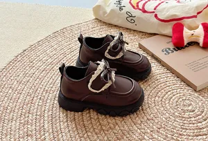 Detail der braunen Mädchenschuhe aus Leder mit Schleife und Spitze auf Strohmatte