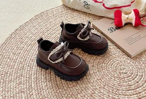 Klassische dunkelbraune Lederschuhe für Mädchen mit Spitzenbogen auf einem Webteppich.