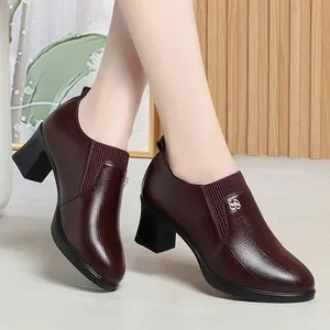 Detail of burgundy pointed-toe block heel loafers on a model with a wooden backdrop.