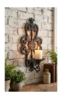 Detailed view of a vintage cast iron wall-mounted candle holder with a lit white pillar candle.