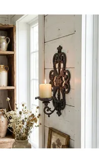 Detailed view of an ornate vintage cast iron wall-mounted candle holder on a white wooden wall