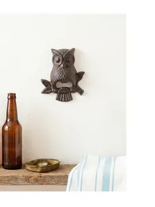 Ouvre-bouteille mural décoratif en fonte en forme de hibou sur un mur blanc texturé.