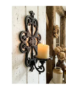 Vintage European cast iron wall sconce with ornate scrollwork holding a lit candle.