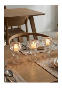 Nahaufnahme von drei gerippten Kerzenhaltern aus Glas auf einem warmen Holzesstisch