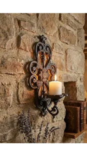 Vintage cast iron wall-mounted candle holder with elegant scrollwork on stone wall