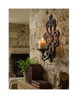 Vintage cast iron wall-mounted candle holder with a lit candle on rustic stone wall