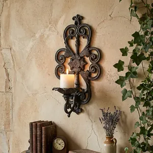 European vintage cast iron hollow wall-mounted candle holder featuring a lit pillar candle.