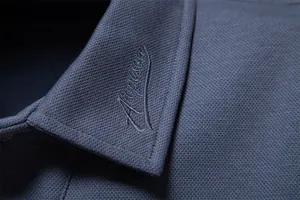 Macro detail of men's navy pique polo shirt collar with elegant signature embroidery