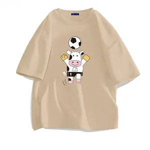 Oversized beige t-shirt featuring a cute cartoon cow playing soccer graphic print
