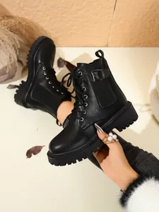 Close-up view of black platform combat boots with metallic buckle and lace-up front design.