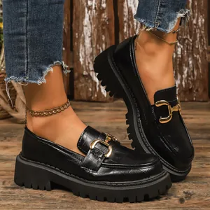 Close-up detail of black platform loafers with crocodile texture and gold buckle