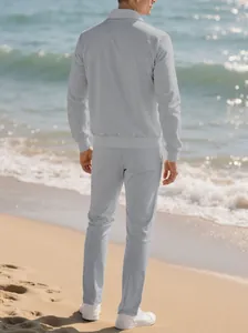 Back view of a man wearing a light gray textured tracksuit on a sunny beach site.