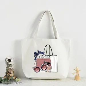 Front view of a white canvas tote bag with fashion-themed graphic print and lifestyle props.