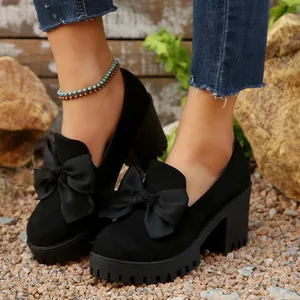 Close-up of black chunky heel platform pumps with a large decorative bow and suede finish.