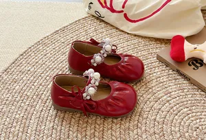 Chaussures Mary Jane rouges pour enfants avec bride en perles et nœud sur tapis de paille