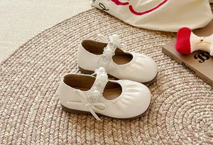 Gros plan de chaussures Mary Jane crème pour enfants avec perles et détails plissés sur un tapis