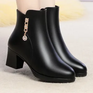 Détail de bottines en cuir souple noir avec breloques dorées et talon bloc épais