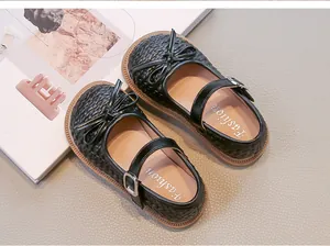 Dettaglio di scarpe Mary Jane intrecciate per bambina in nero con fiocco e fibbia.