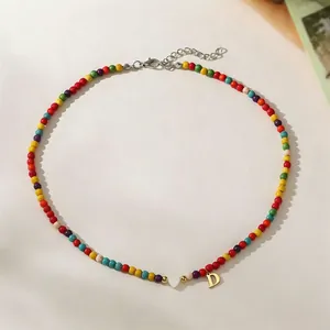 Close-up detail of colorful bead necklace featuring a gold letter D and white heart pendant charm
